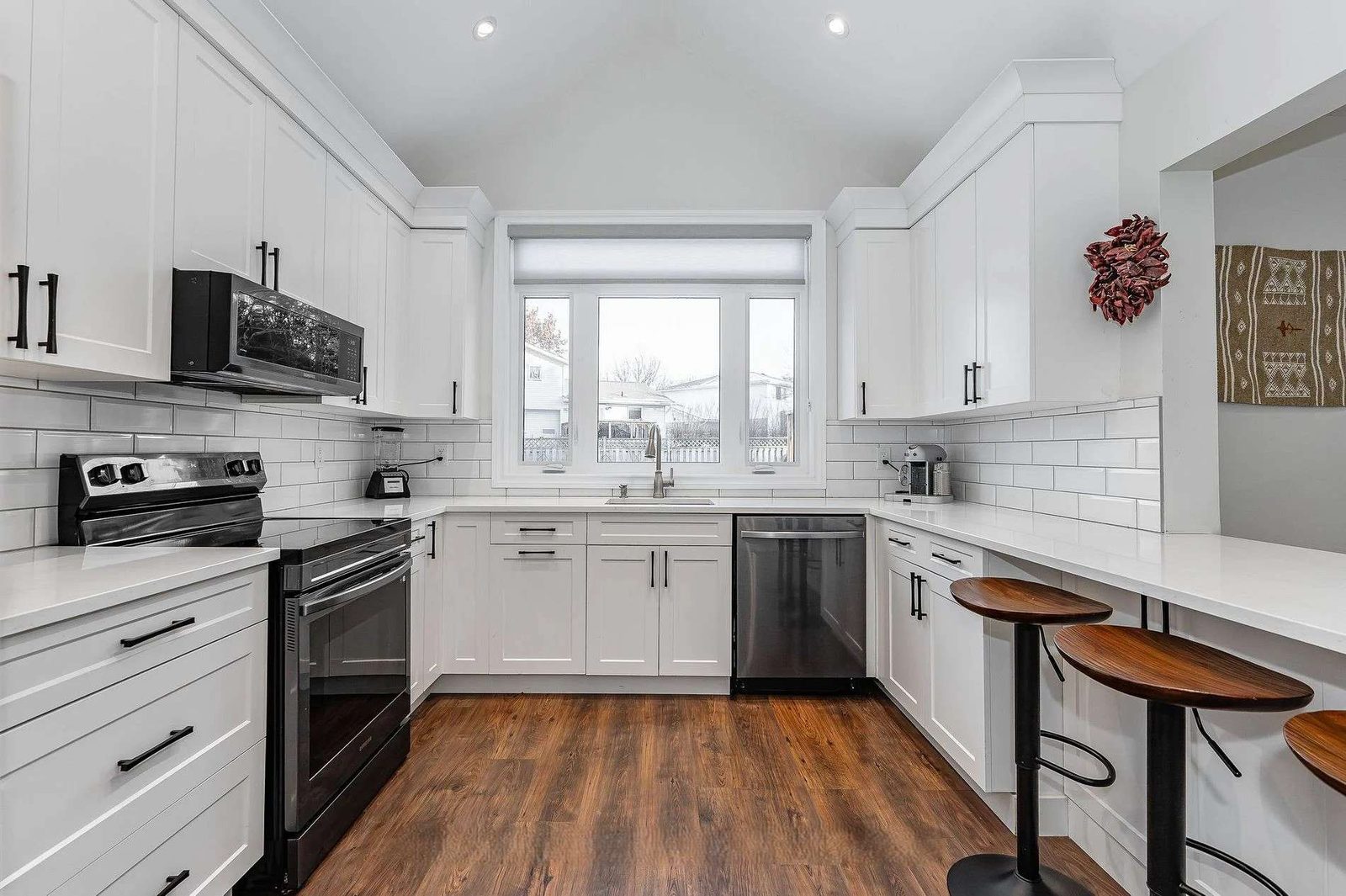 Bright white kitchen renovation with a black island, brass pendant lights and warm wood flooring